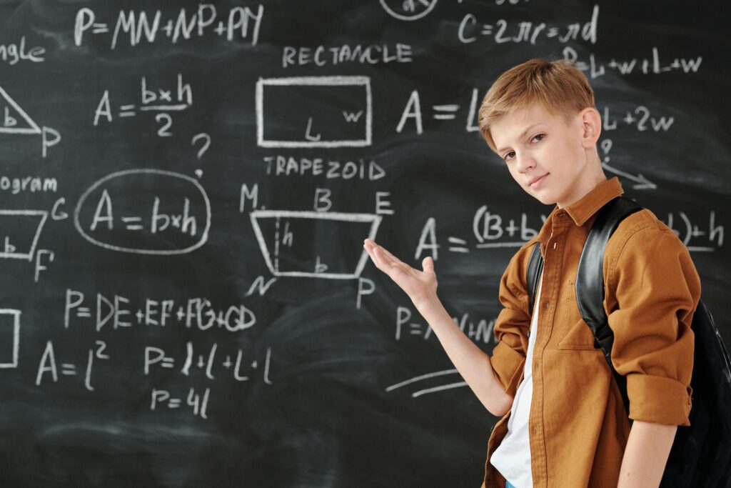 A young student confidently demonstrating geometric formulas on a classroom blackboard.